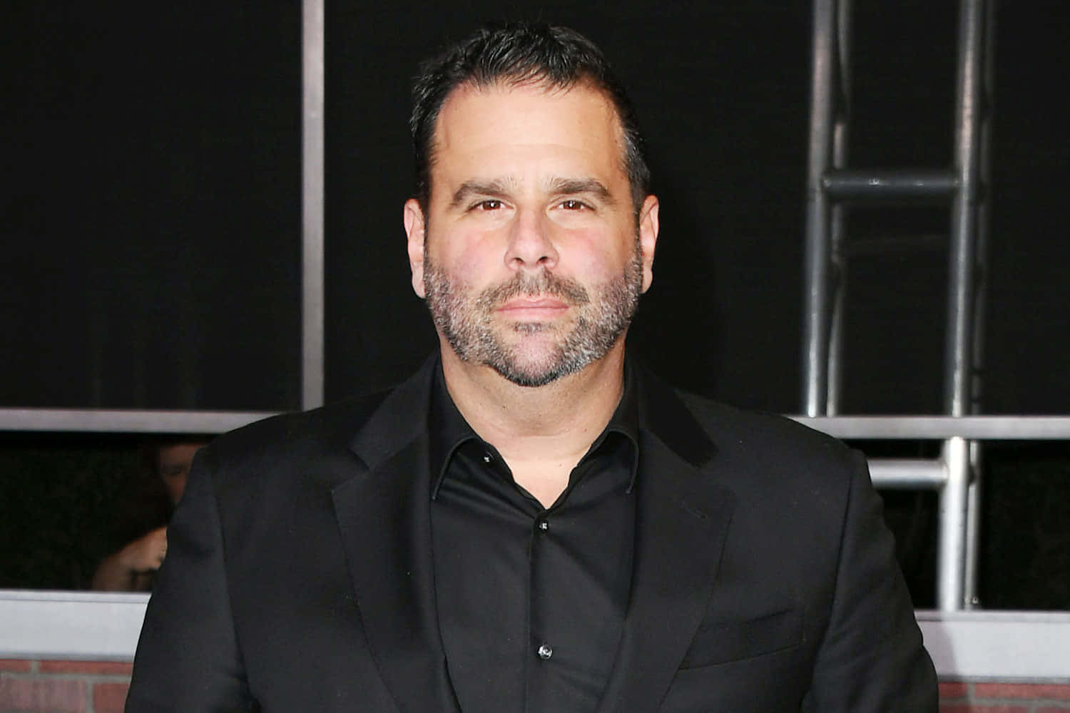 A Man In A Black Suit Standing On A Red Carpet