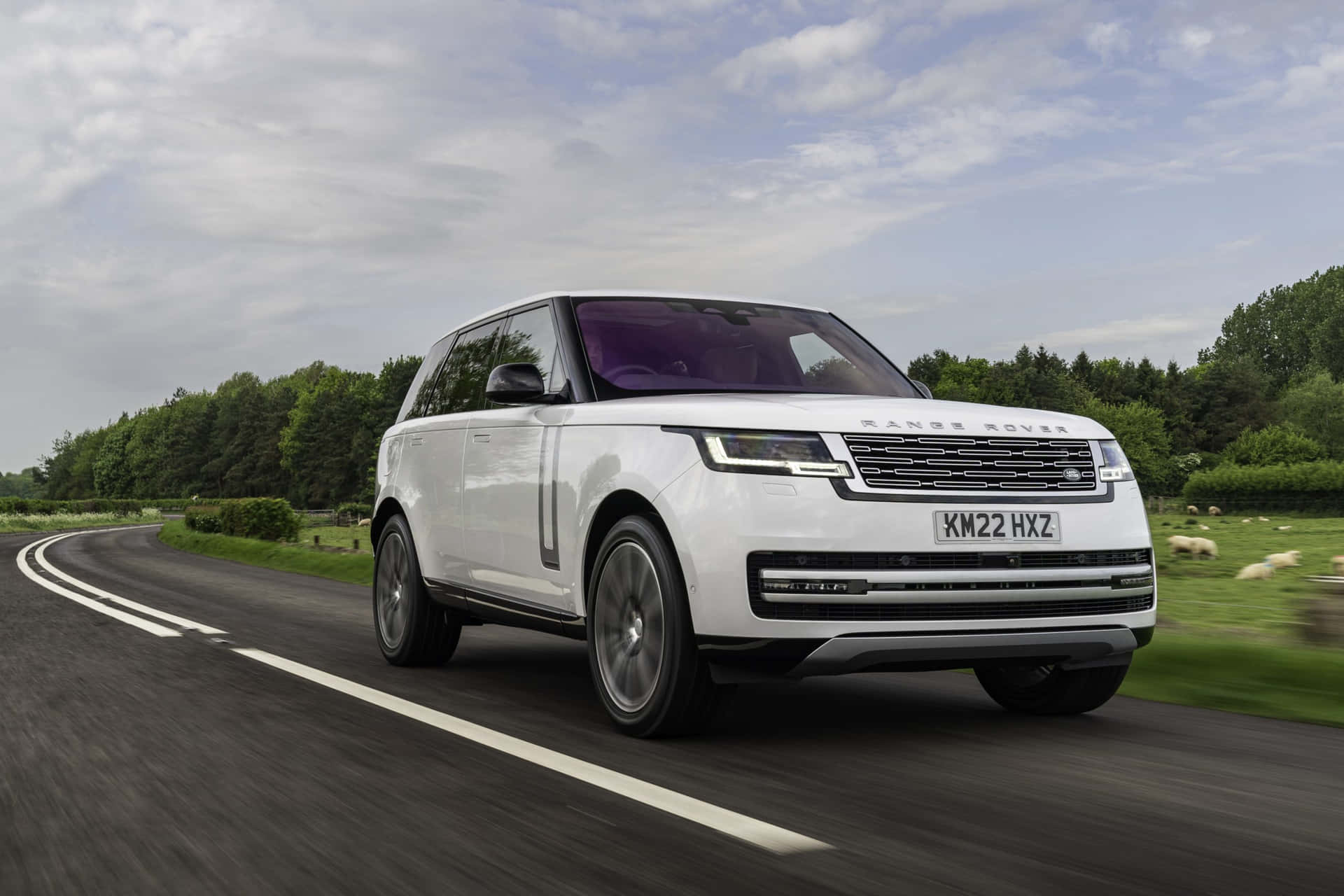 The White Range Rover Is Driving Down A Country Road
