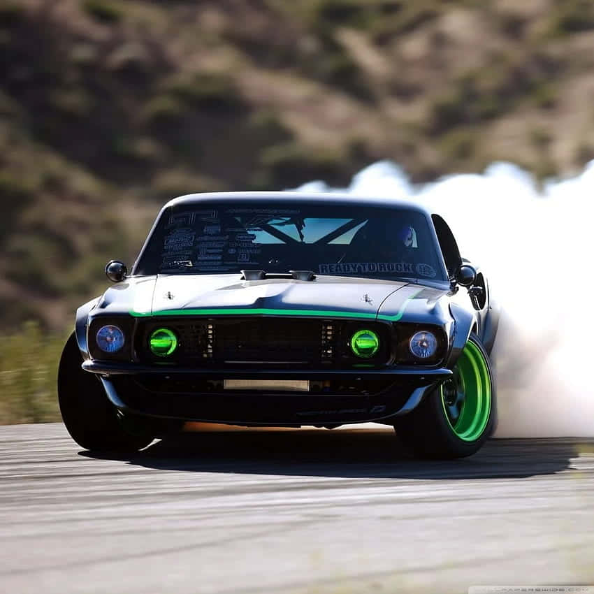 A Black Mustang Is Driving Down A Track With Green Lights Wallpaper