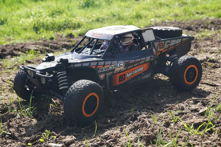 A Black And Orange Rc Off Road Truck In The Field Wallpaper