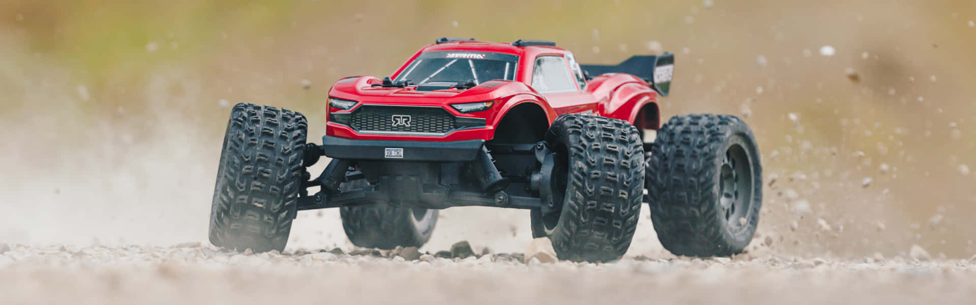 A Red Remote Control Truck Is Driving On A Dirt Road
