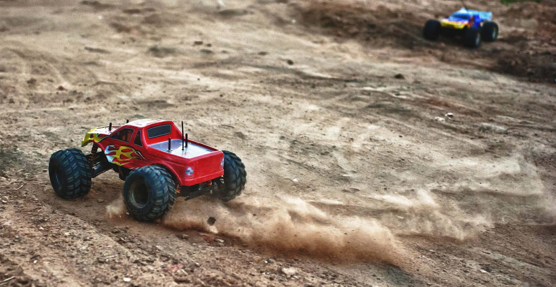 Two Red Monster Trucks Are Driving Down A Dirt Road