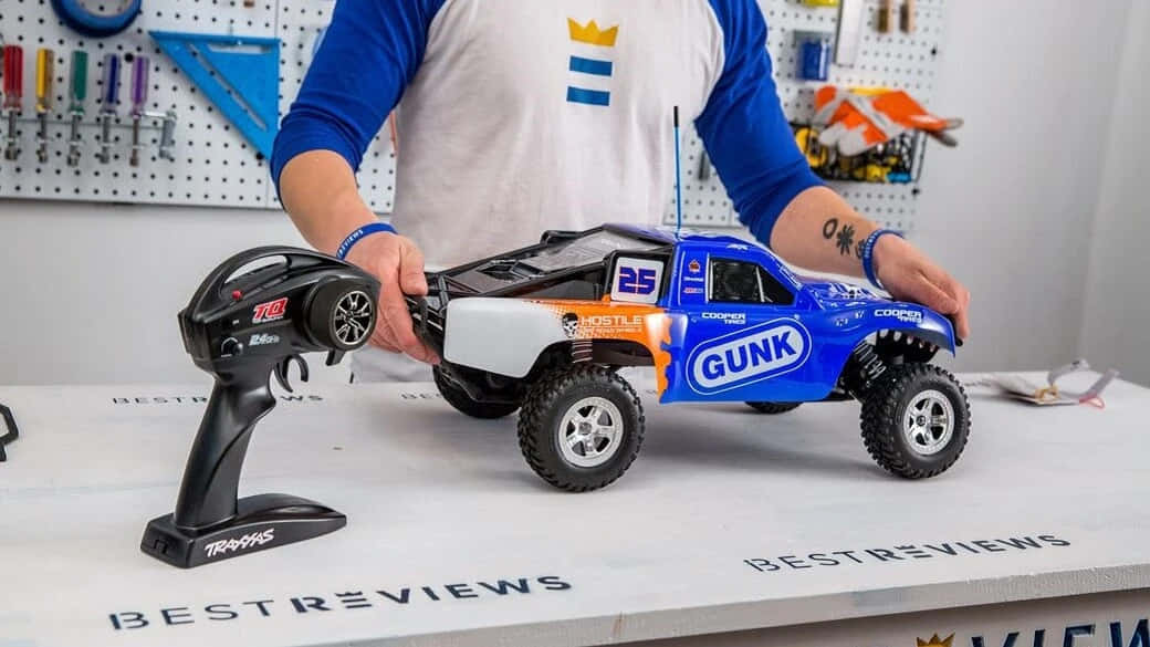 A Man Is Holding A Blue Toy Truck On A Table
