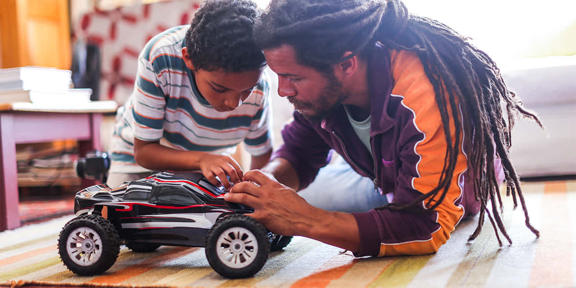 A Man And His Son Playing With A Toy Car