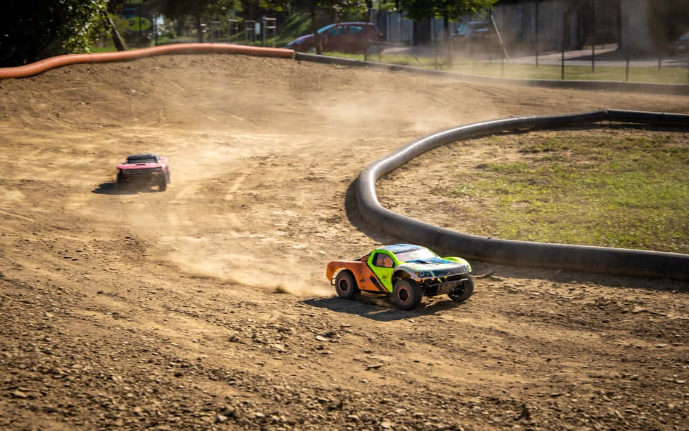 Two Toy Trucks Are Racing Down A Dirt Track
