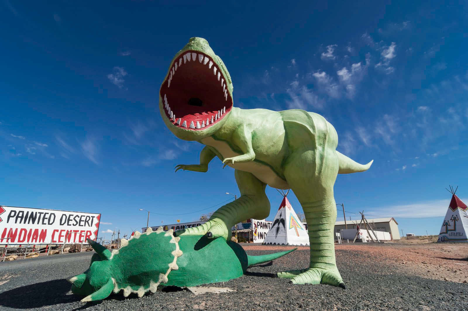 En stor dinosaur statue er foran en teepee
