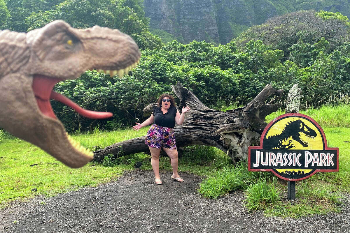 Unamujer Está Parada Frente A Un Letrero De Jurassic Park.