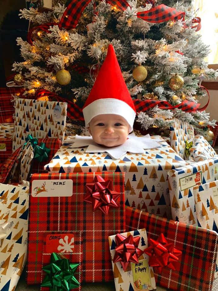 A Baby In A Elf Hat Sitting In Front Of A Christmas Tree