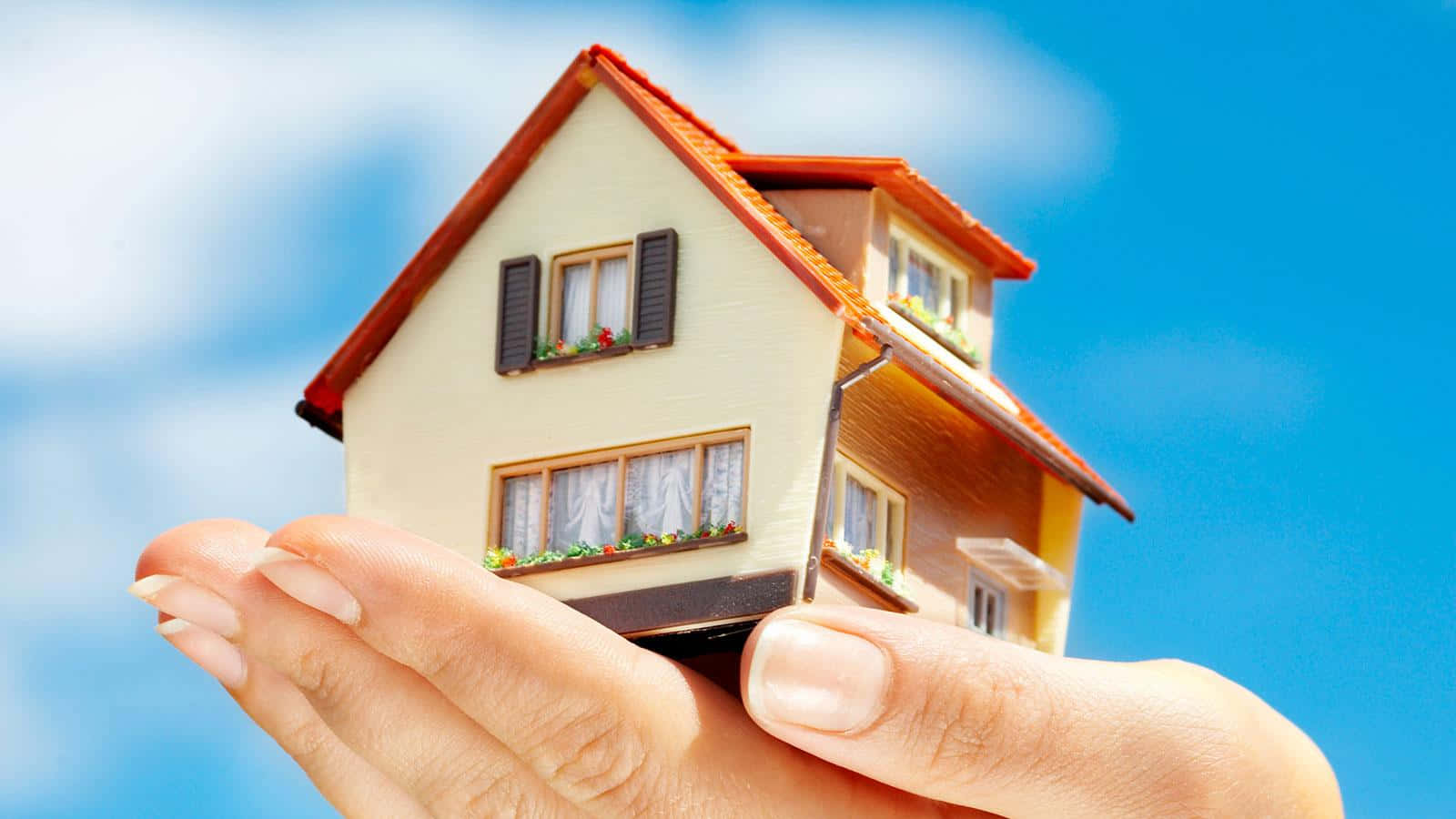 A Person Holding A Model House In Their Hand