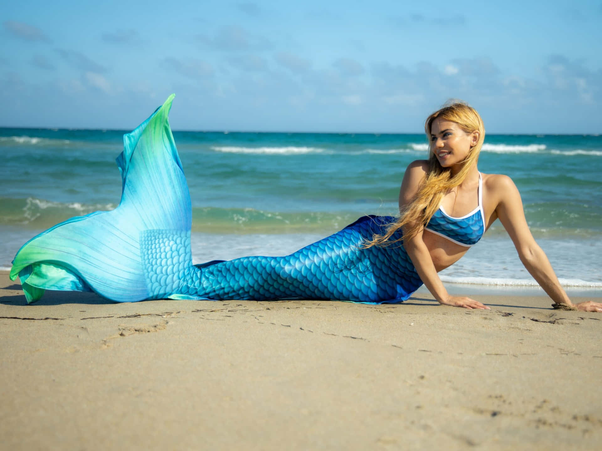 A Beautiful Woman In A Blue Mermaid Tail Laying On The Beach