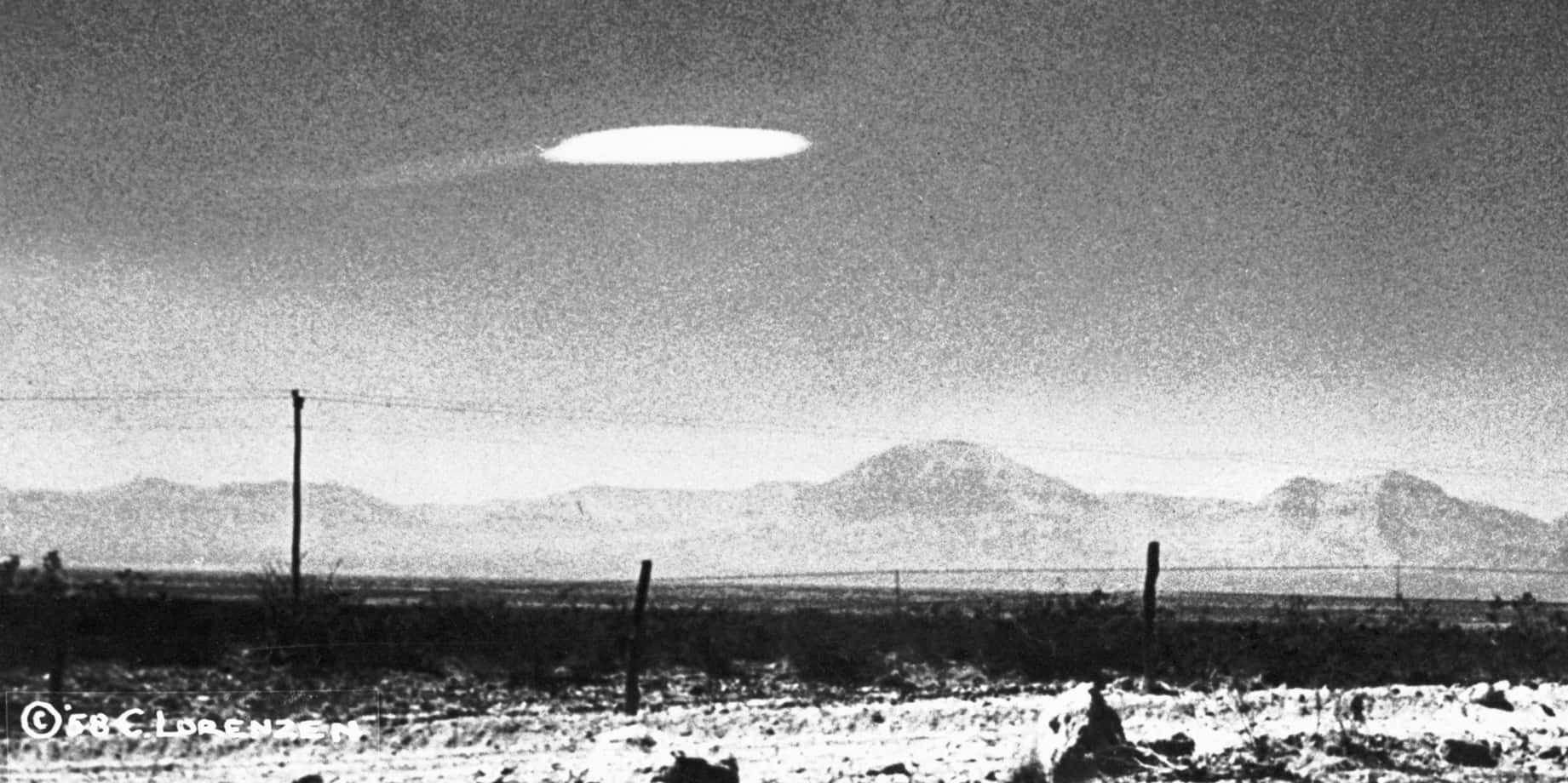 A Black And White Photo Of An Ufo Flying Over A Field