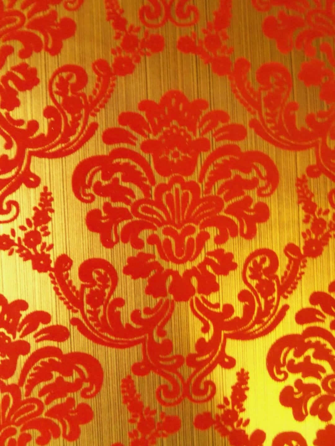 Et rødt og guldt damask tapet, der skimrer i lyset Wallpaper