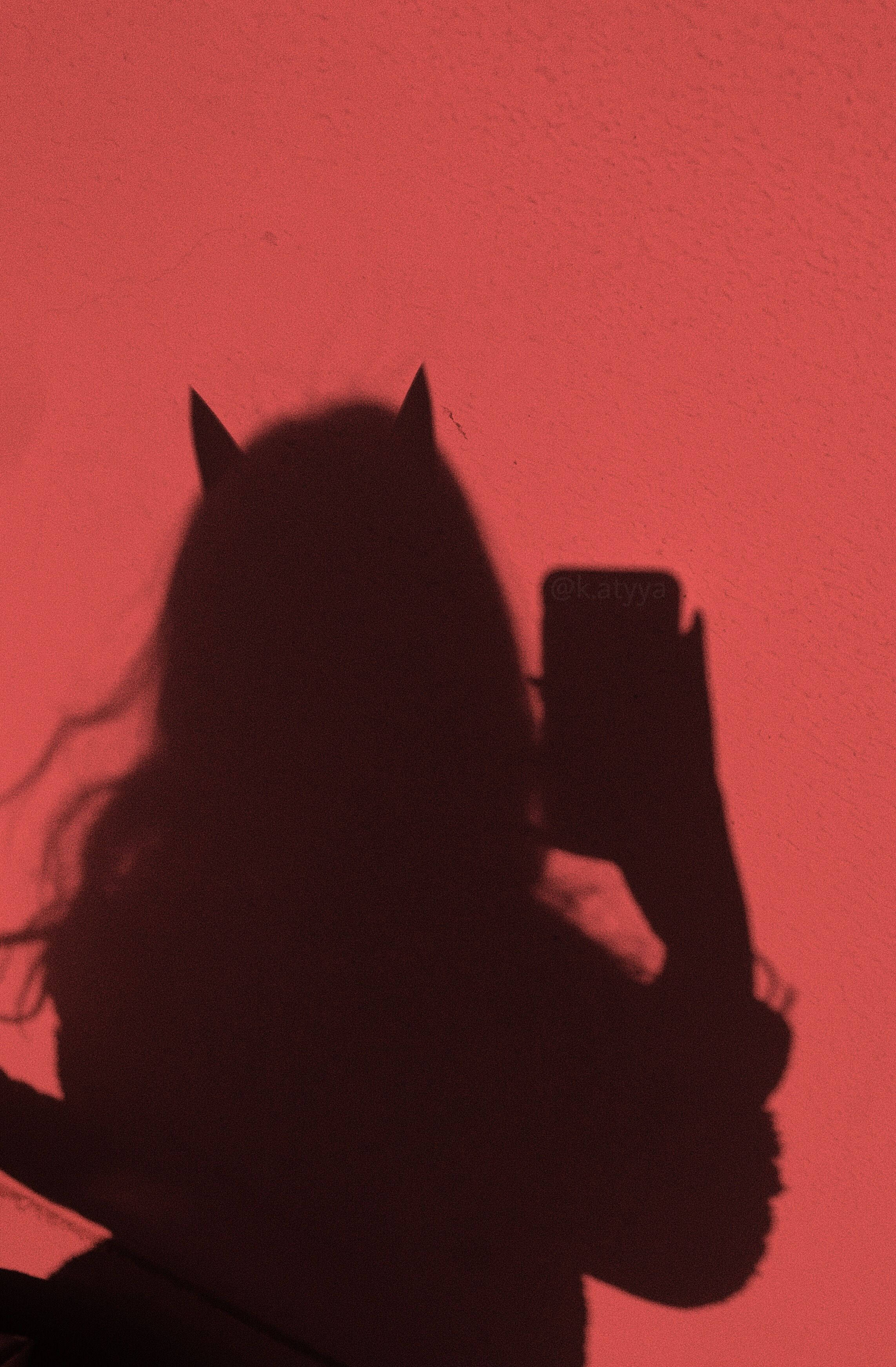 Tempting Red Devil Girl Wallpaper — A dramatic red-lit shadow of a person with devil horns taking a selfie against a textured wall.