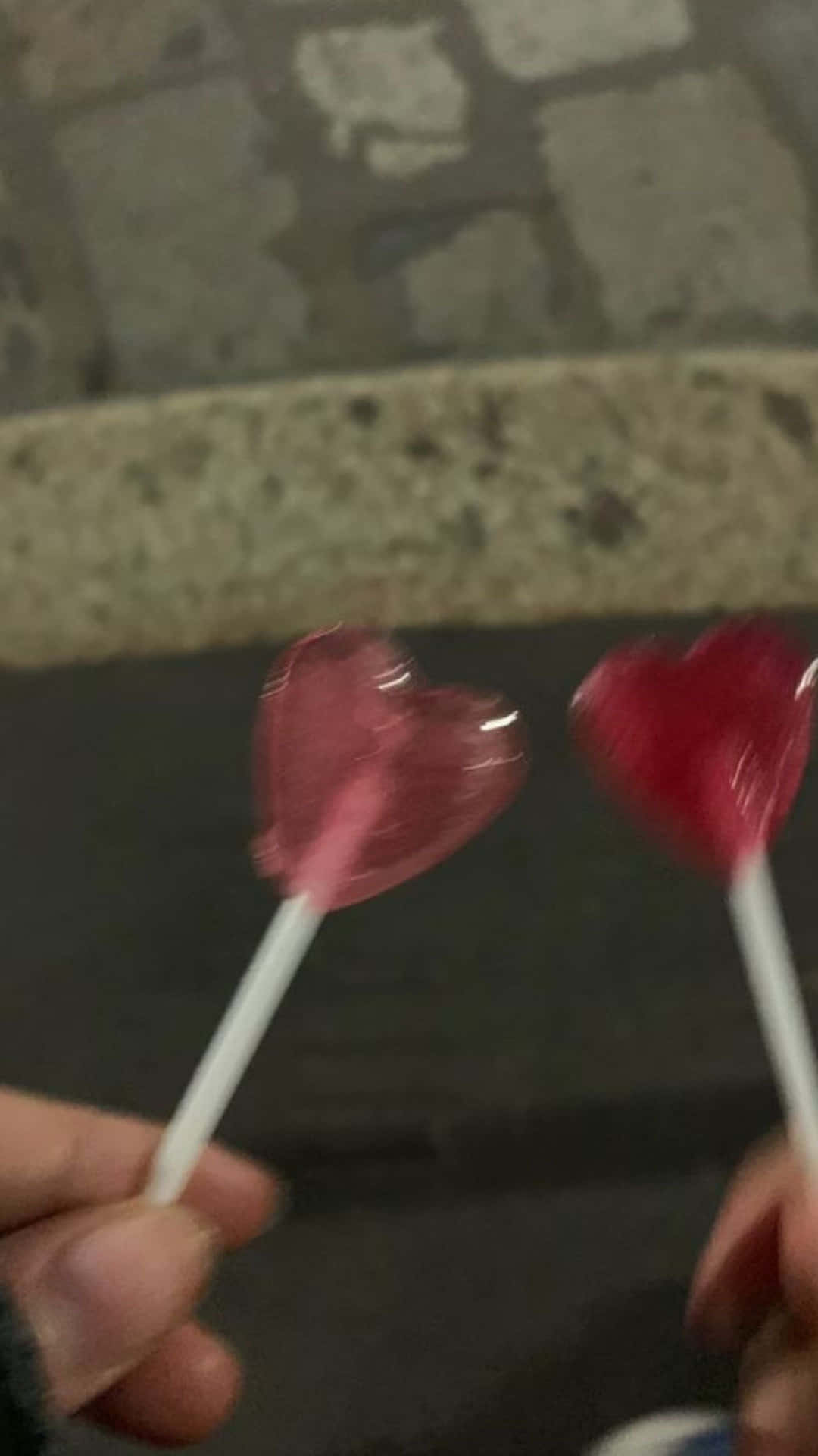 two people holding two heart shaped lollipops
