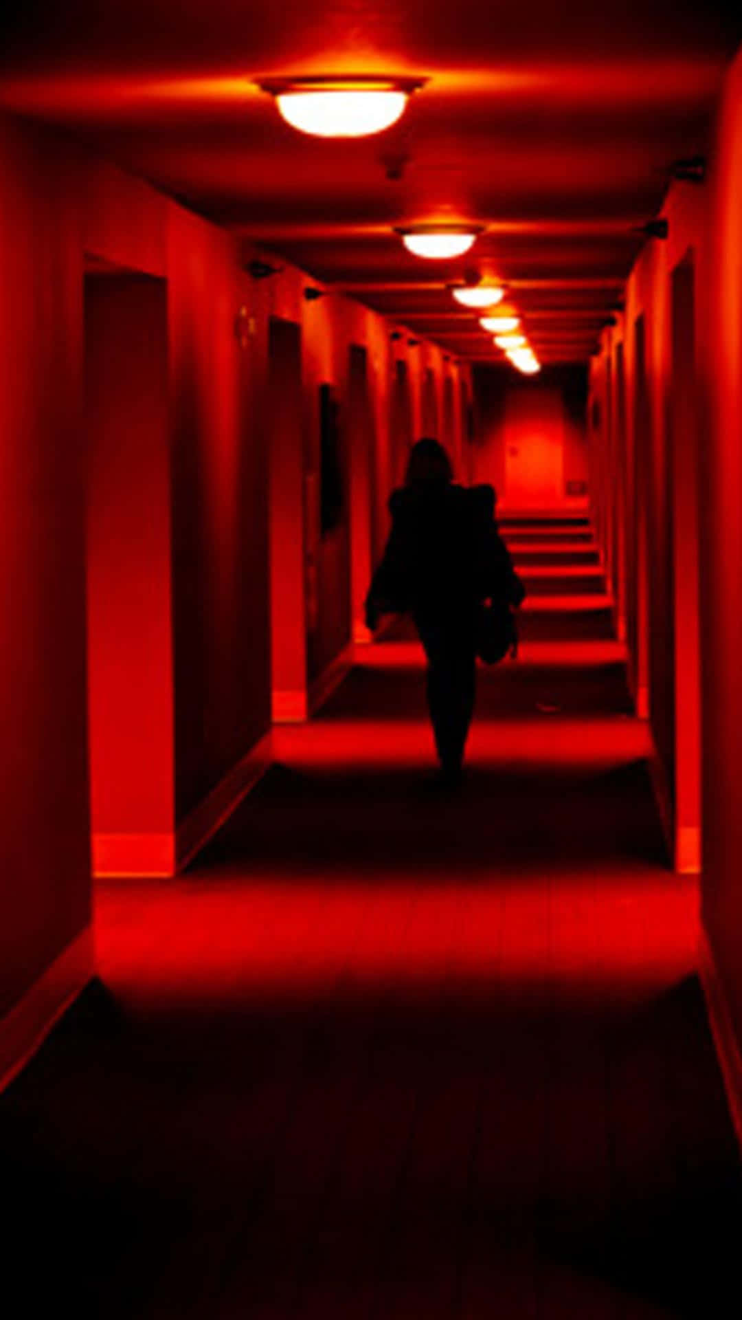 A Person Walking Down A Hallway With Red Lights