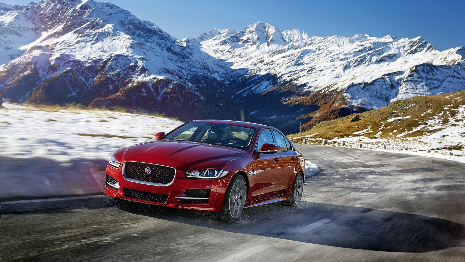 En rød Jaguar bil kører hurtigt gennem et bjerglandskab. Wallpaper