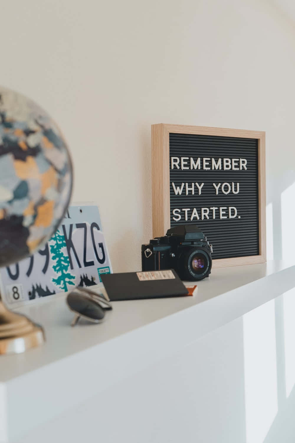 A Shelf With A Camera, A Globe, And A Sign That Says Remember Why You Started