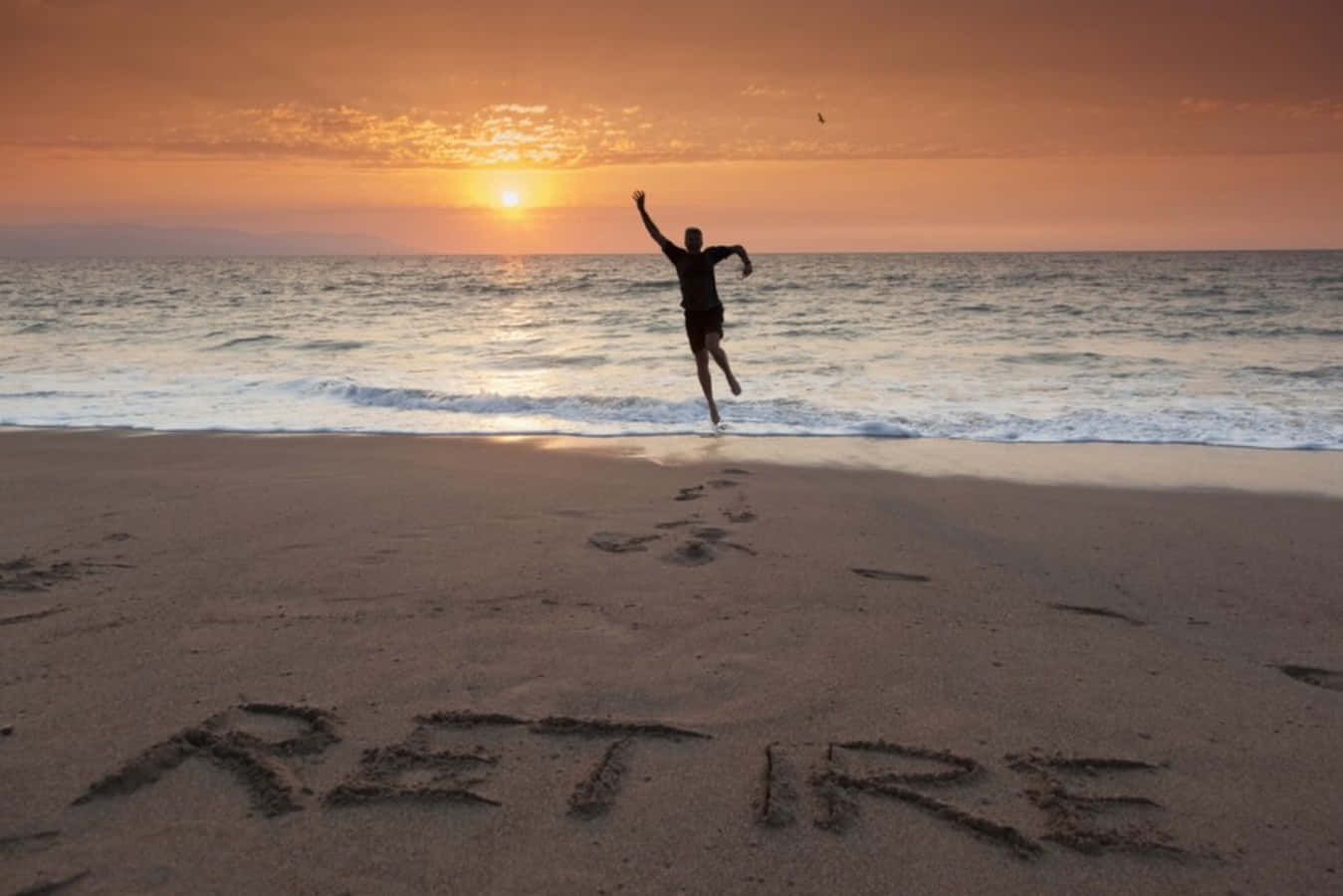 a man jumping on the beach with the word retire written in sand