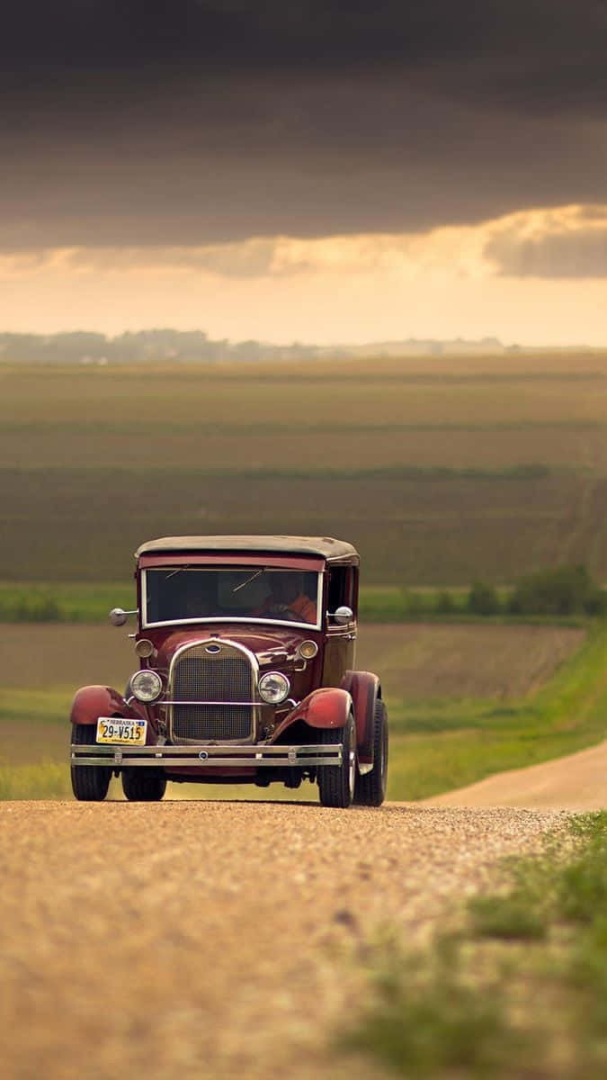 A Red Old Car Driving Down A Dirt Road Wallpaper