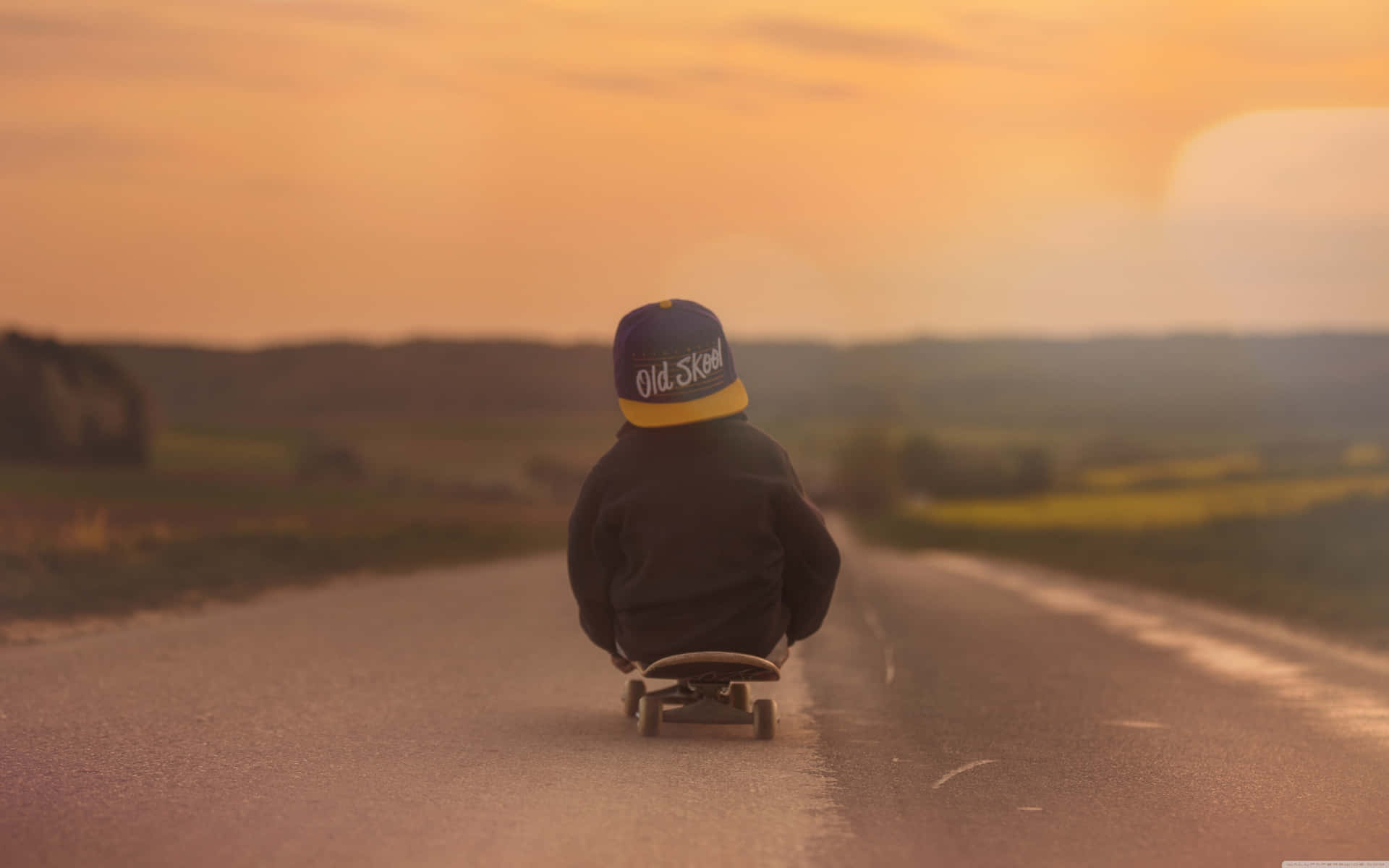 En dreng rider en skateboard ned ad en vej ved solnedgang Wallpaper