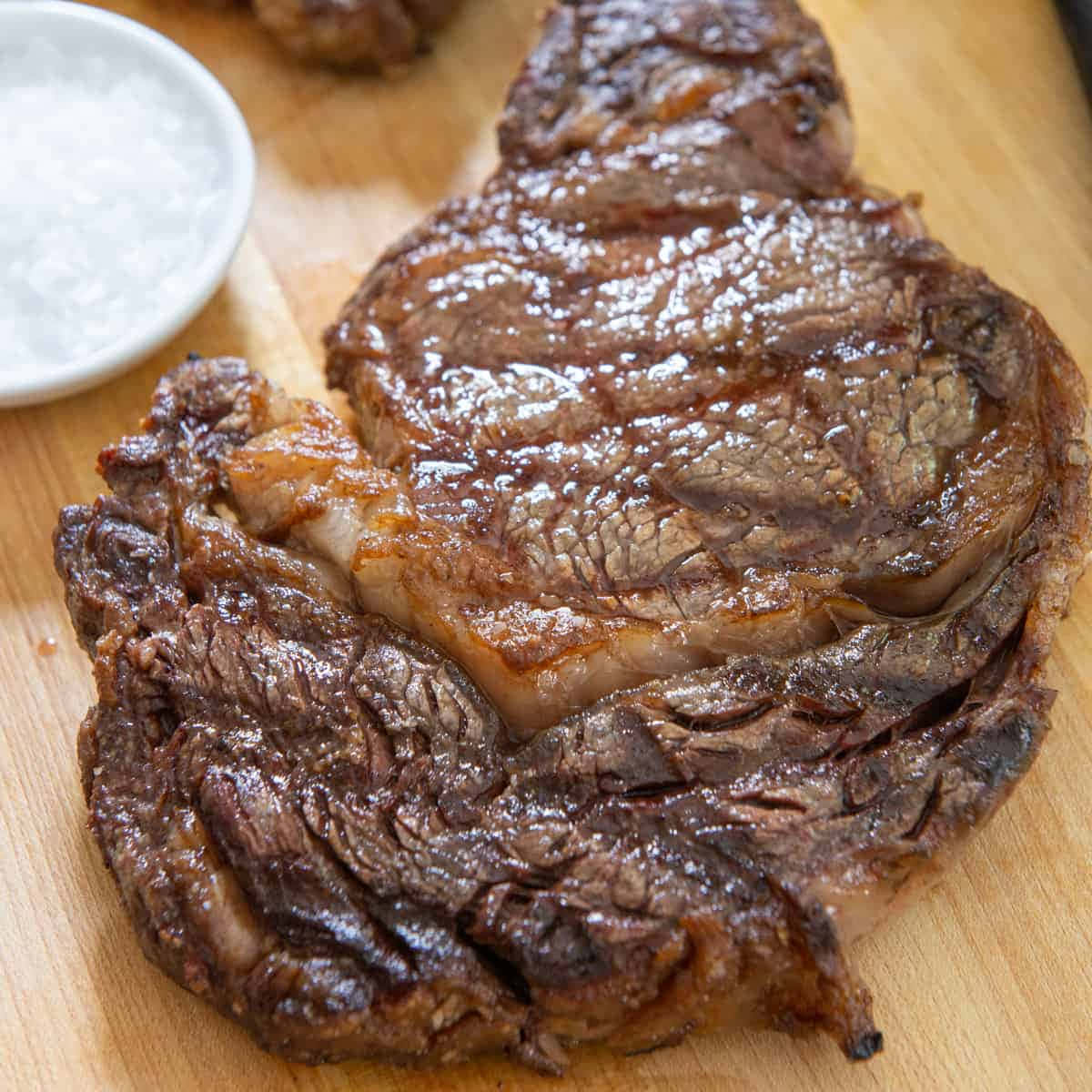 A Steak On A Cutting Board With Salt And Pepper