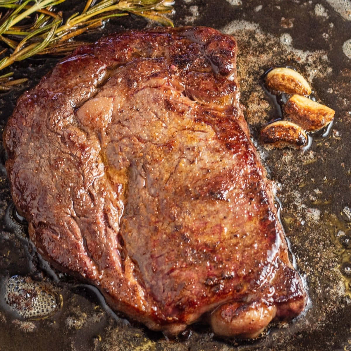 A Steak Is Being Cooked In A Pan With Rosemary