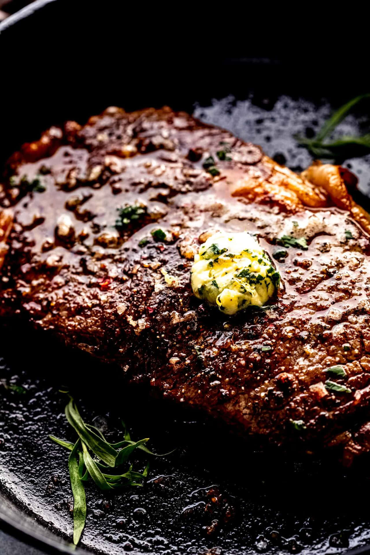 A Steak Is In A Skillet With Butter And Herbs