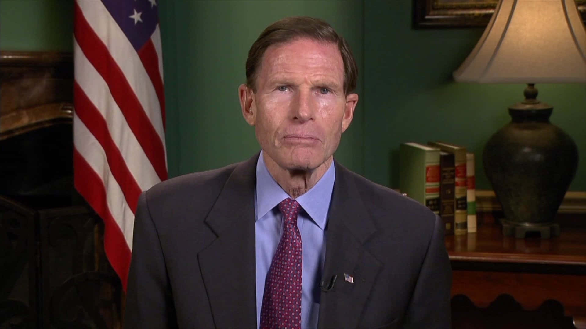 Senator Richard Blumenthal posed against a green backdrop and an American flag Wallpaper