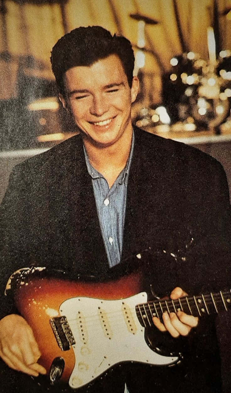 A Man Is Smiling While Holding A Guitar