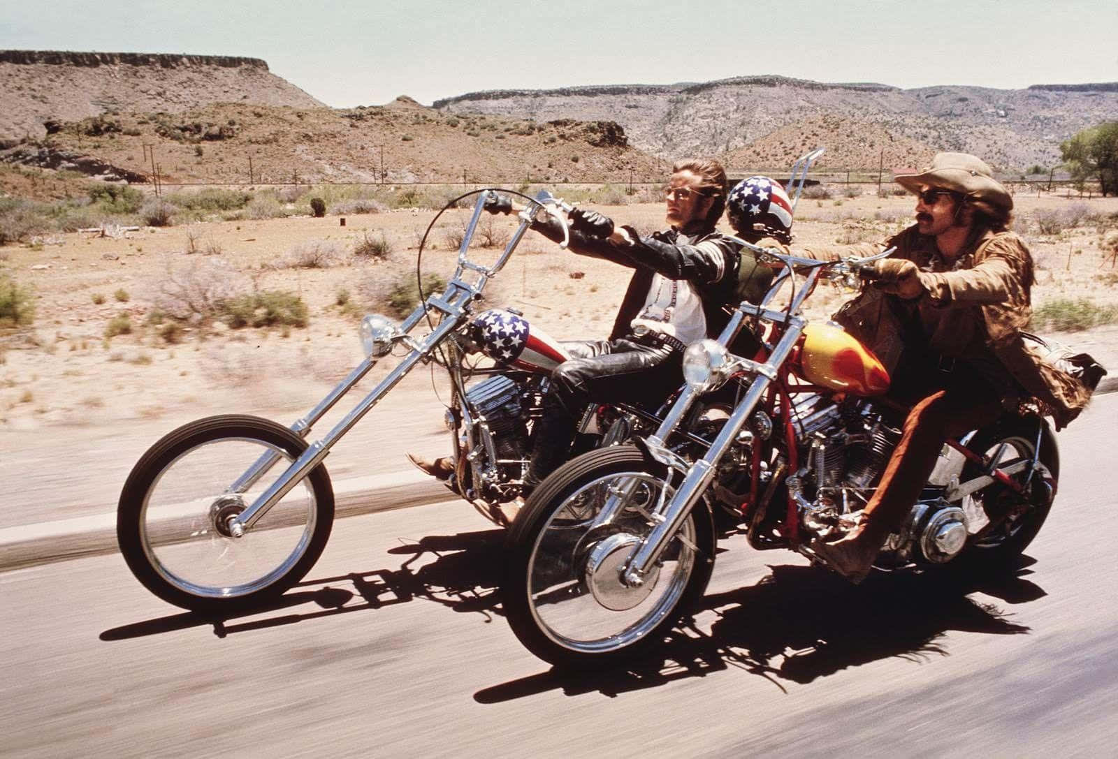 Two Men Riding Motorcycles Down A Desert Road