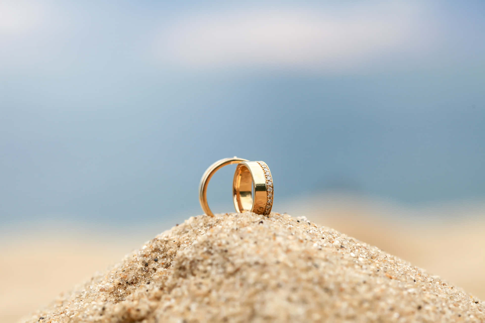 Two Wedding Rings On A Sand Dune With The Ocean In The Background