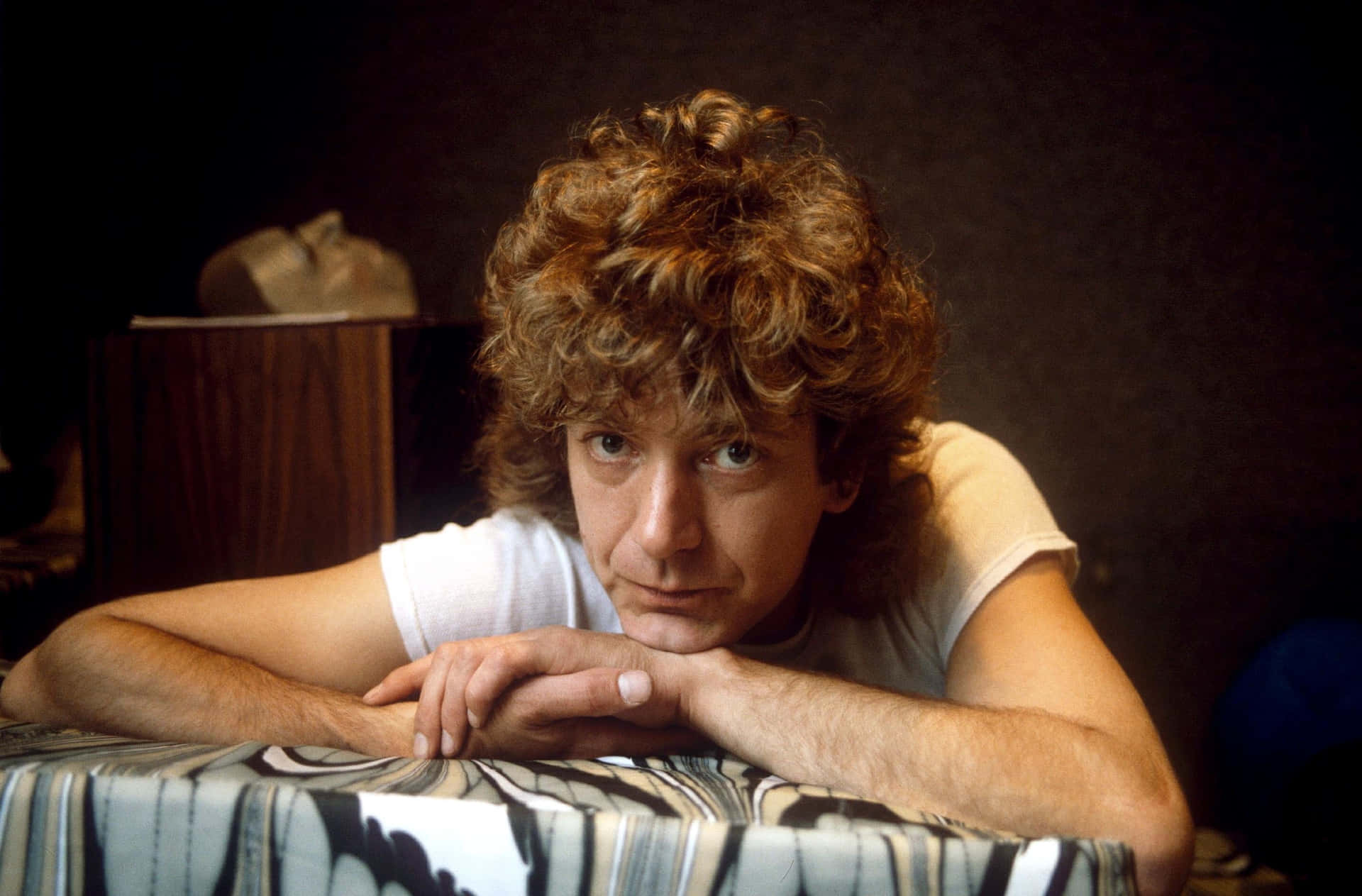 A Man With Curly Hair Leaning On A Bed