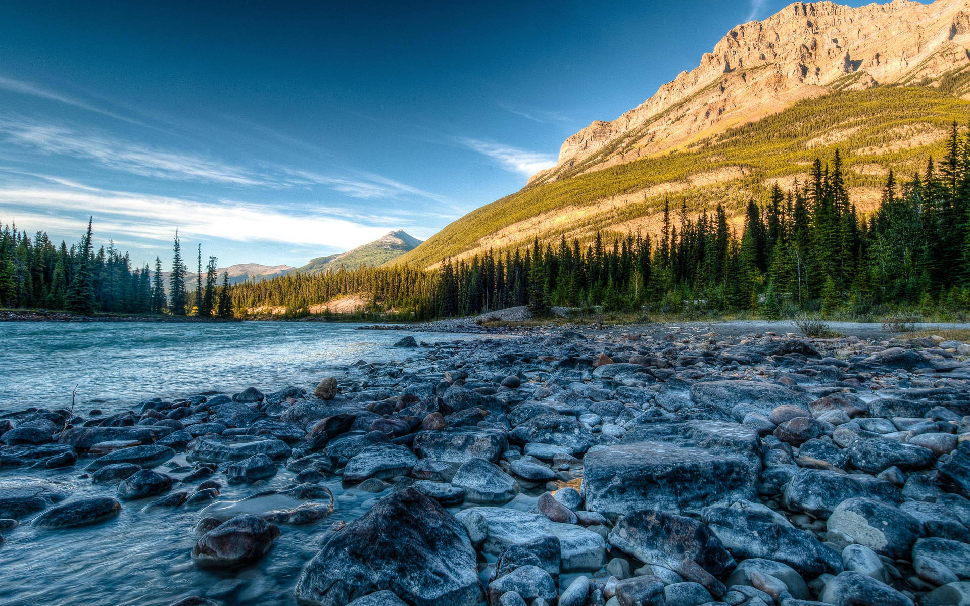 Majestic Rocky Mountain landscape featuring a serene lake and a stone covered shoreline Wallpaper