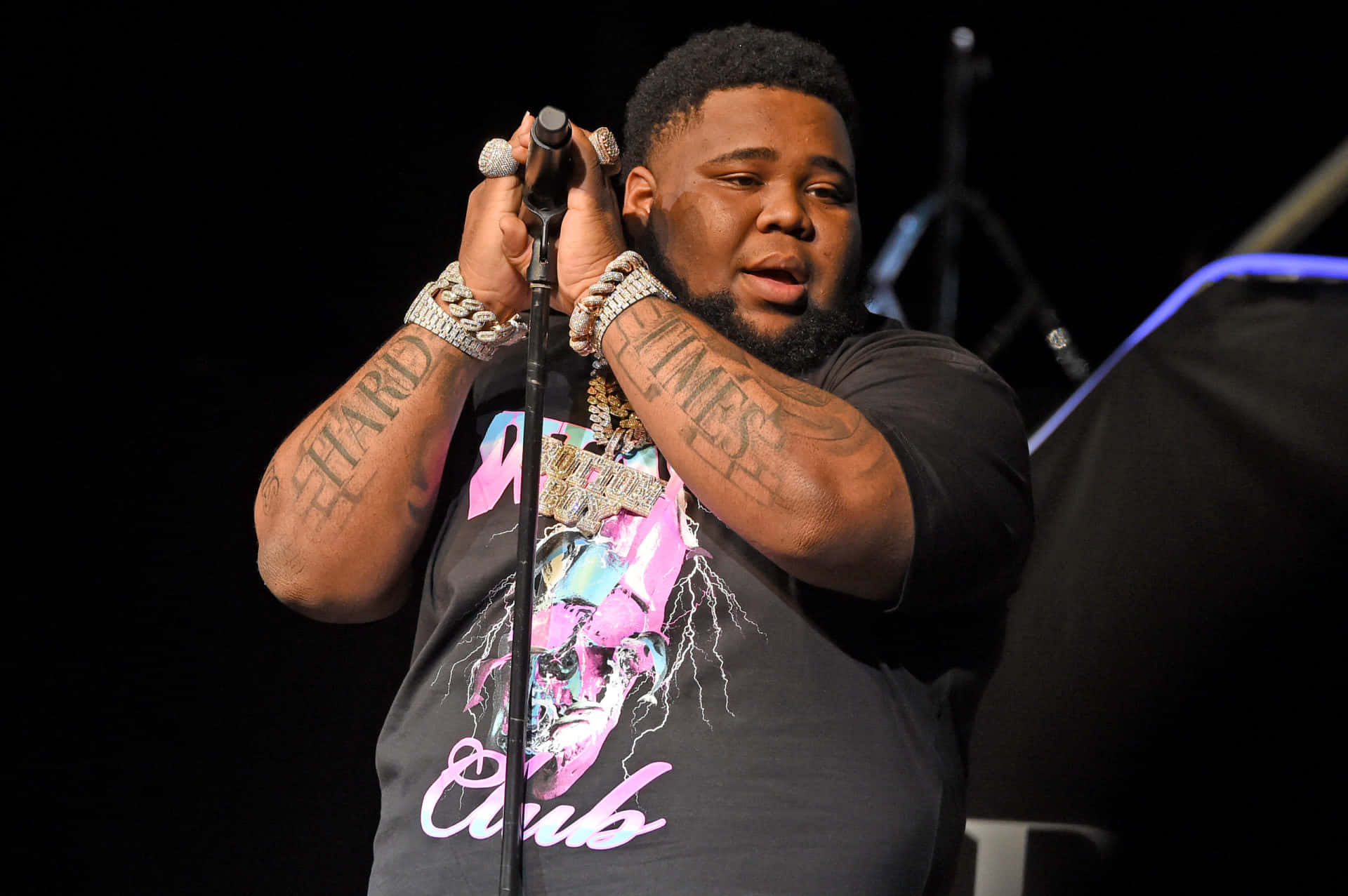 A Man With Tattoos On His Arms Is Holding A Microphone