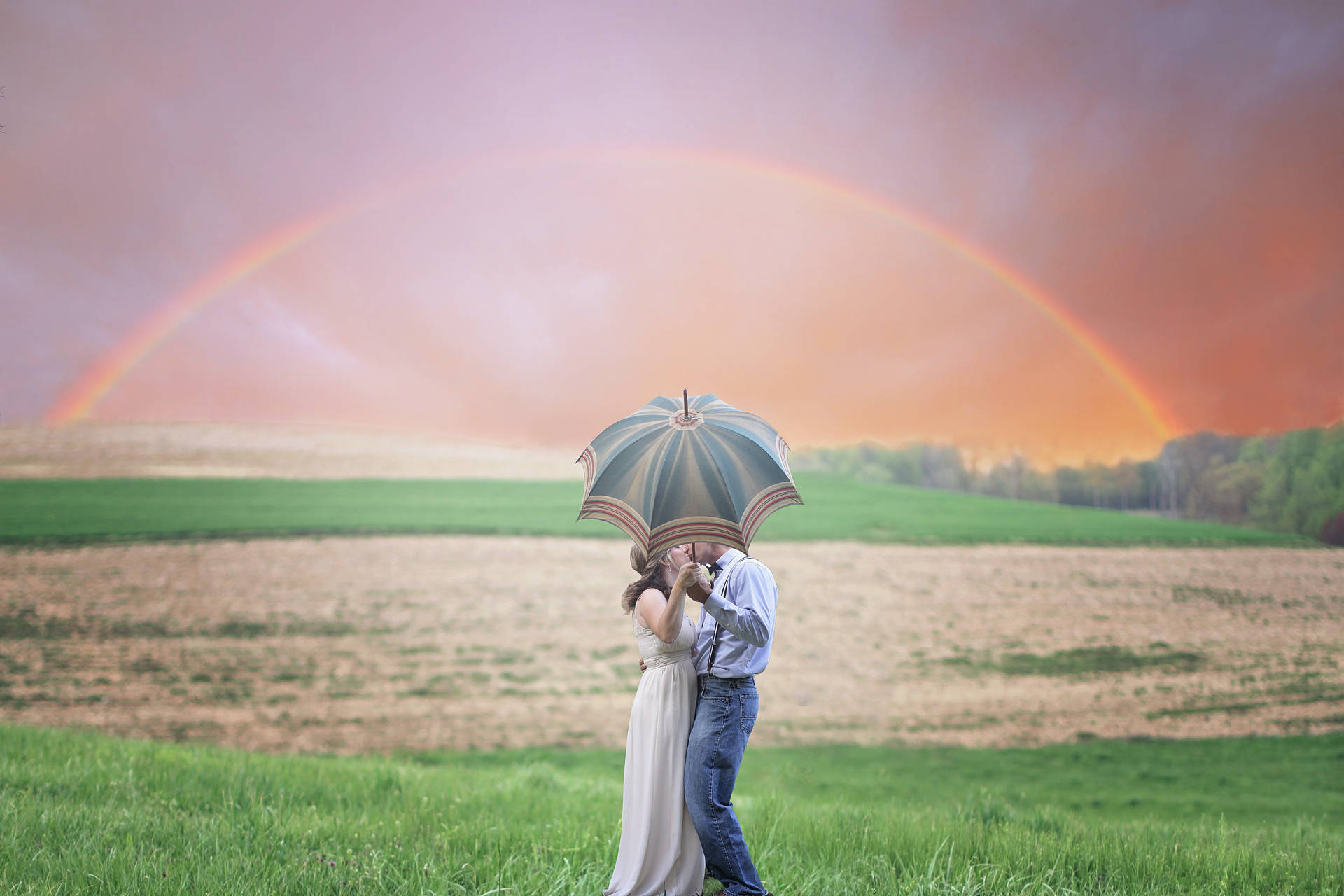 Romantisktpar Kysser Bakom Paraply Under Regnbågen. Wallpaper