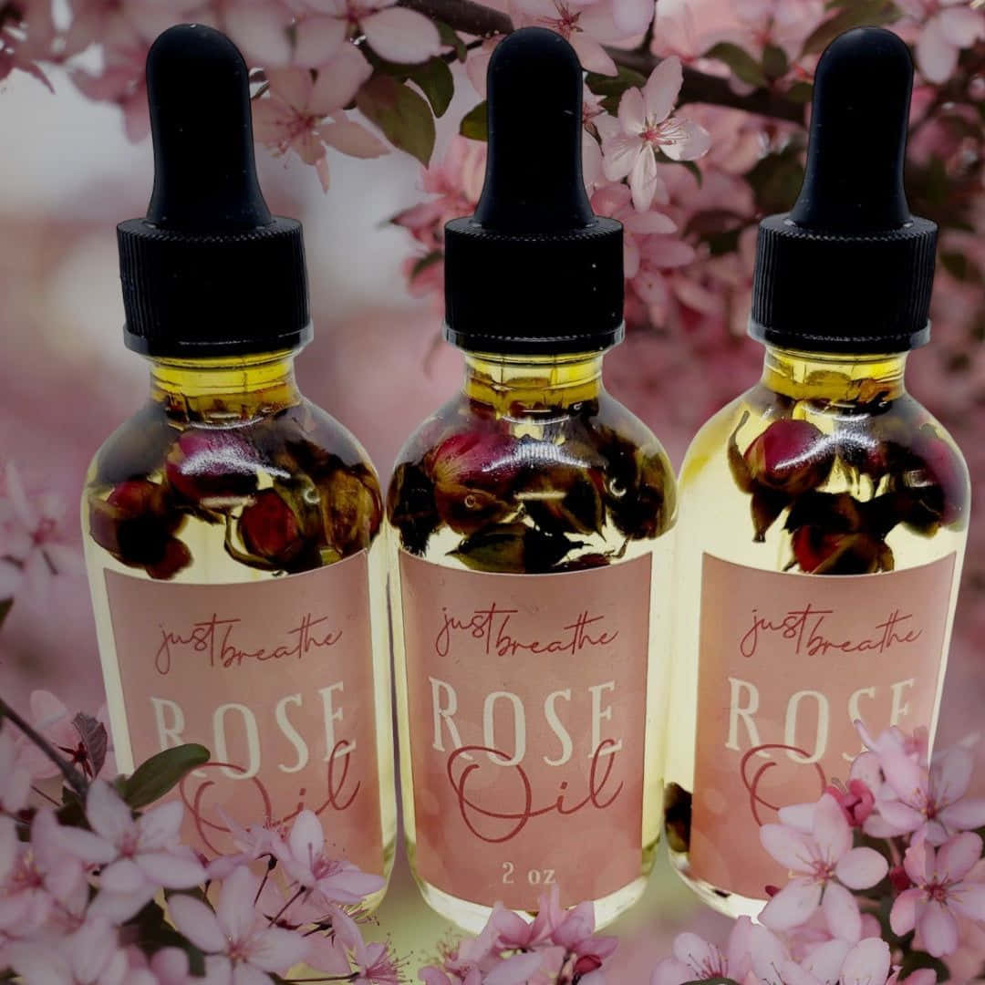 A Beautiful Bottle of Pure Rose Oil Surrounded by Fresh Roses Wallpaper