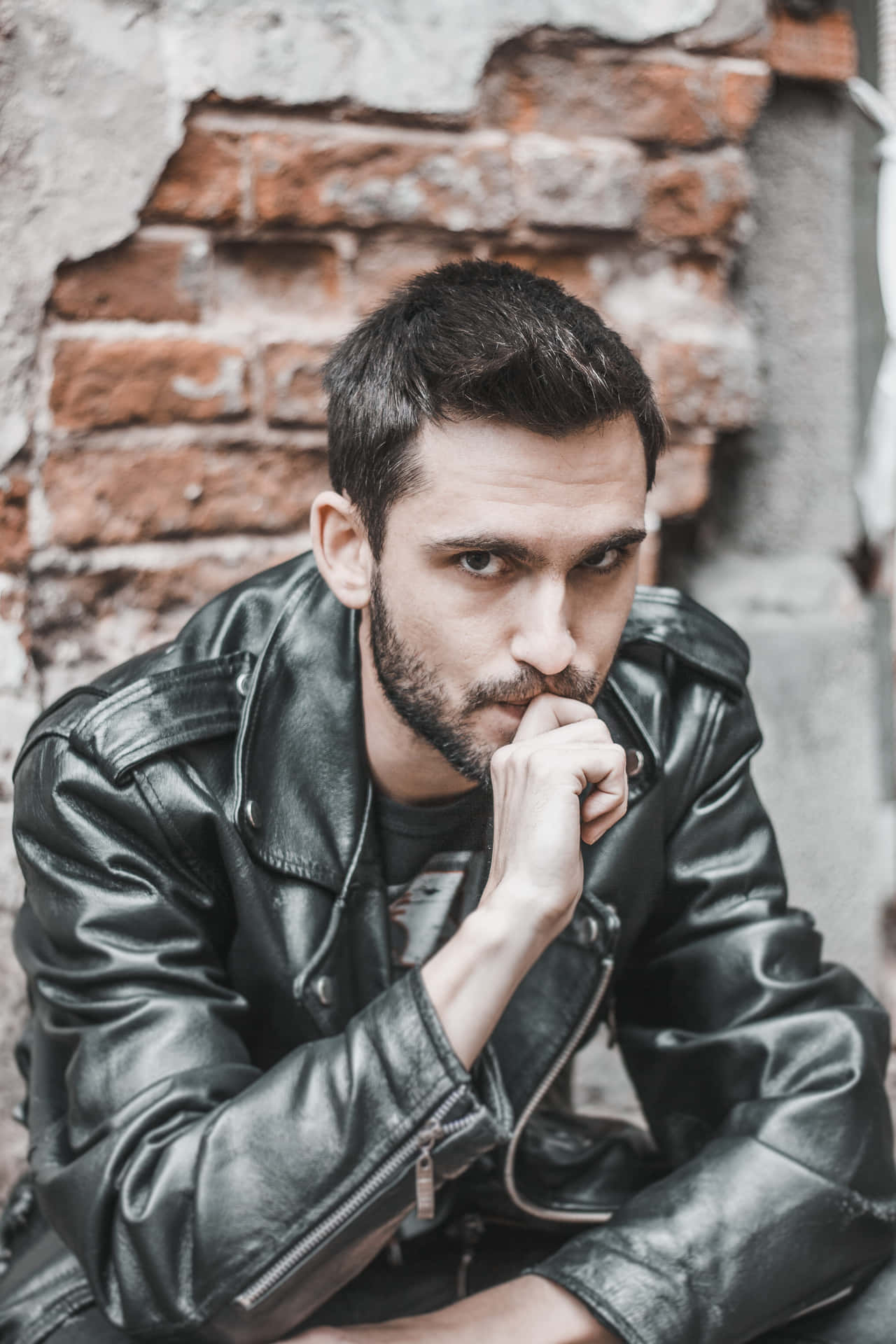 A Man In A Leather Jacket Is Sitting On A Brick Wall Wallpaper