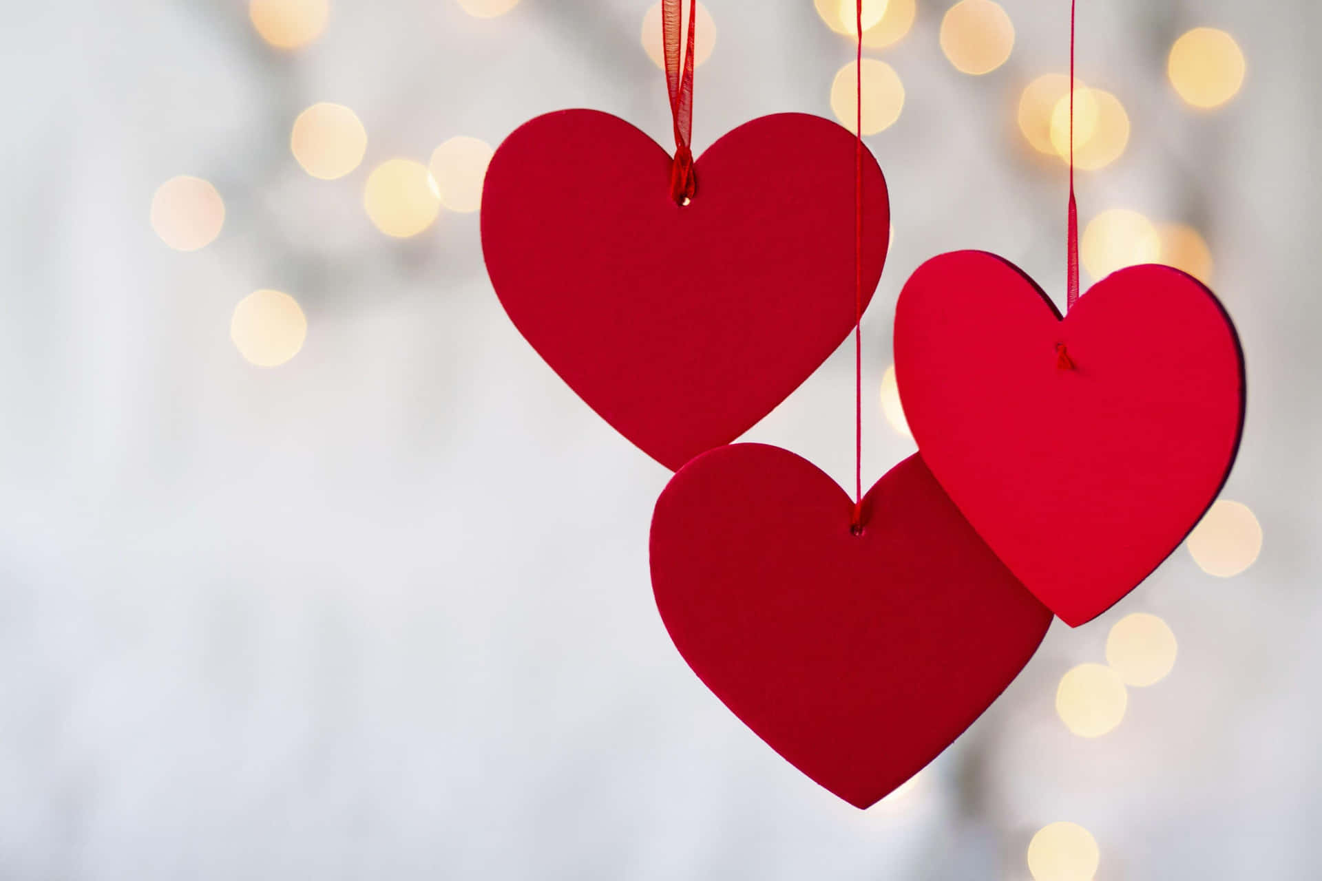 Three Red Hearts Hanging From Strings With Lights Behind Them Wallpaper