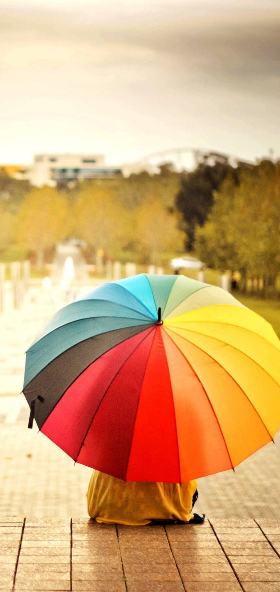 Caption: Vibrant Rainbow Umbrella Against Cloudy Sky Wallpaper