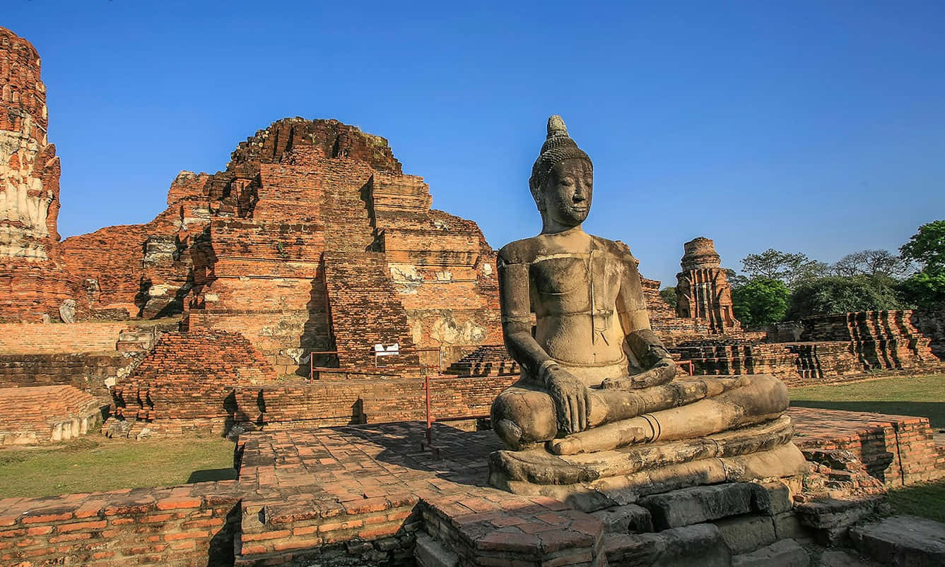 Sacred Buddha Statue Amidst The Historic Ruins Of Ayutthaya Historical Park Wallpaper