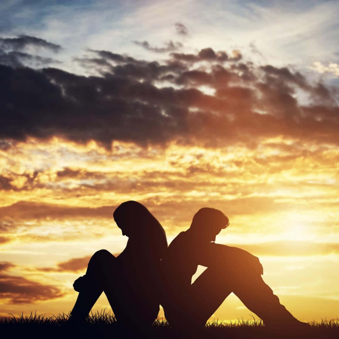 Two People Sitting On A Grassy Field At Sunset