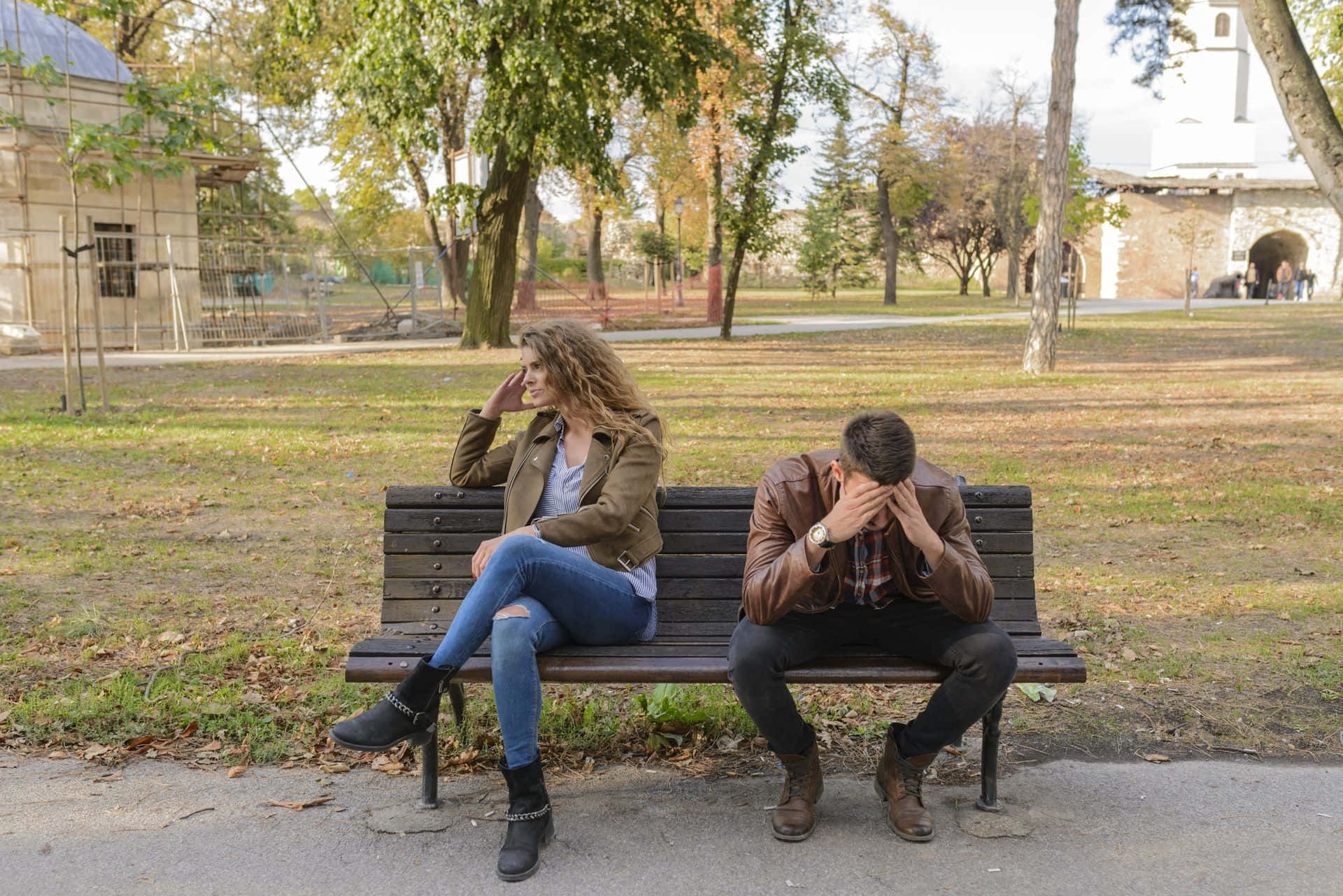 A Man And Woman Sitting On A Bench In A Park