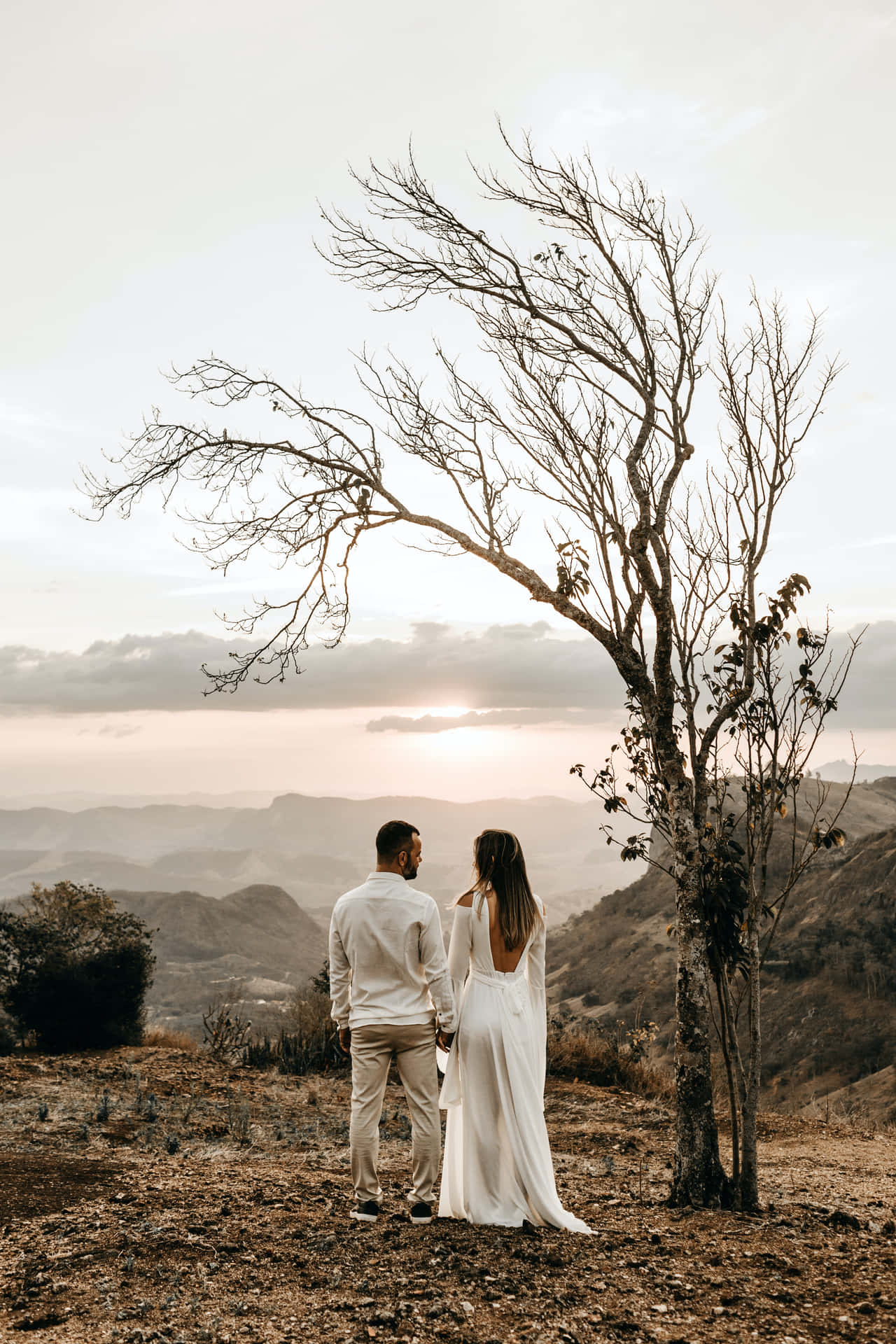 A Bride And Groom Standing On A Hill Overlooking The Mountains Wallpaper