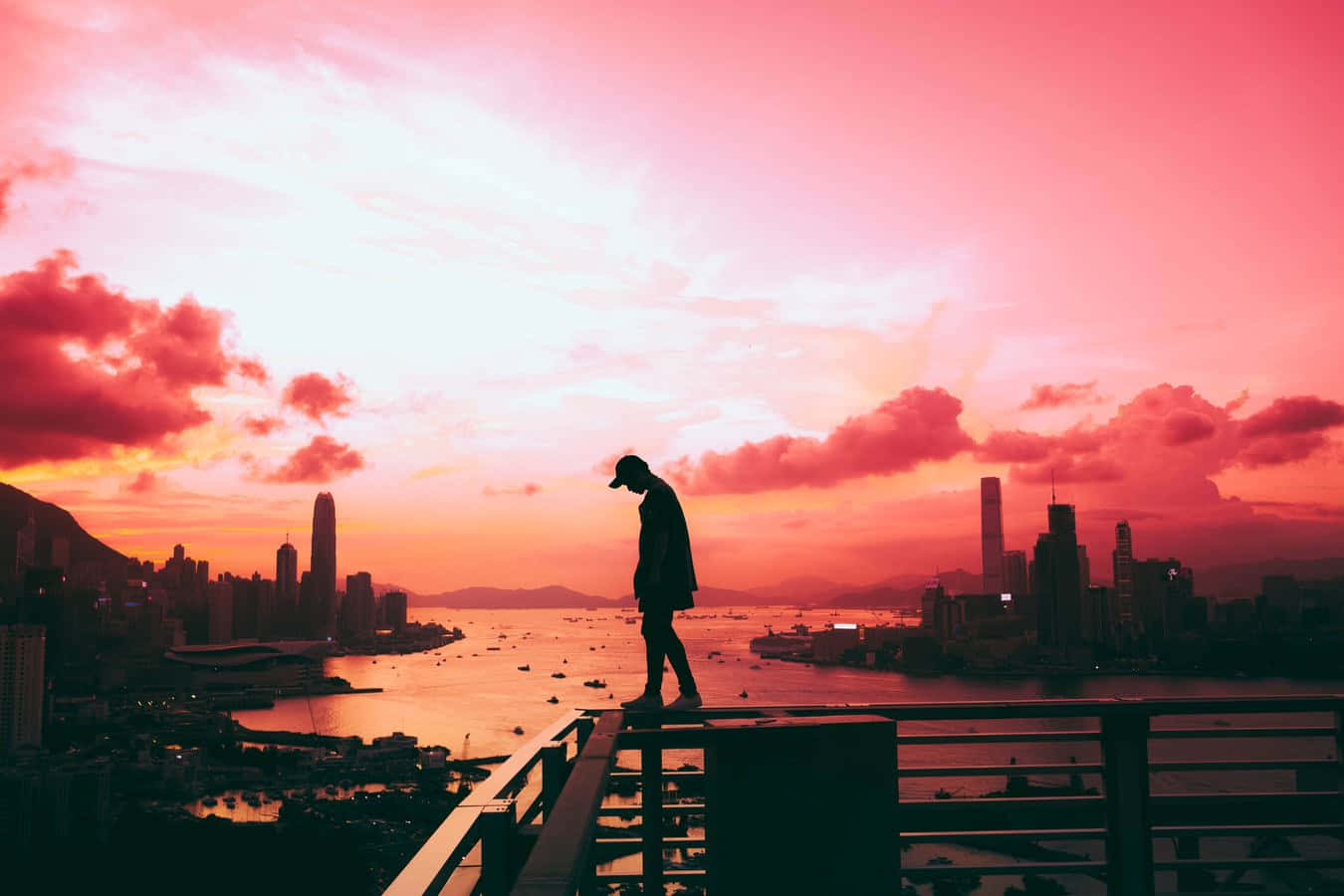 A Person Standing On A Ledge Overlooking A City At Sunset Wallpaper