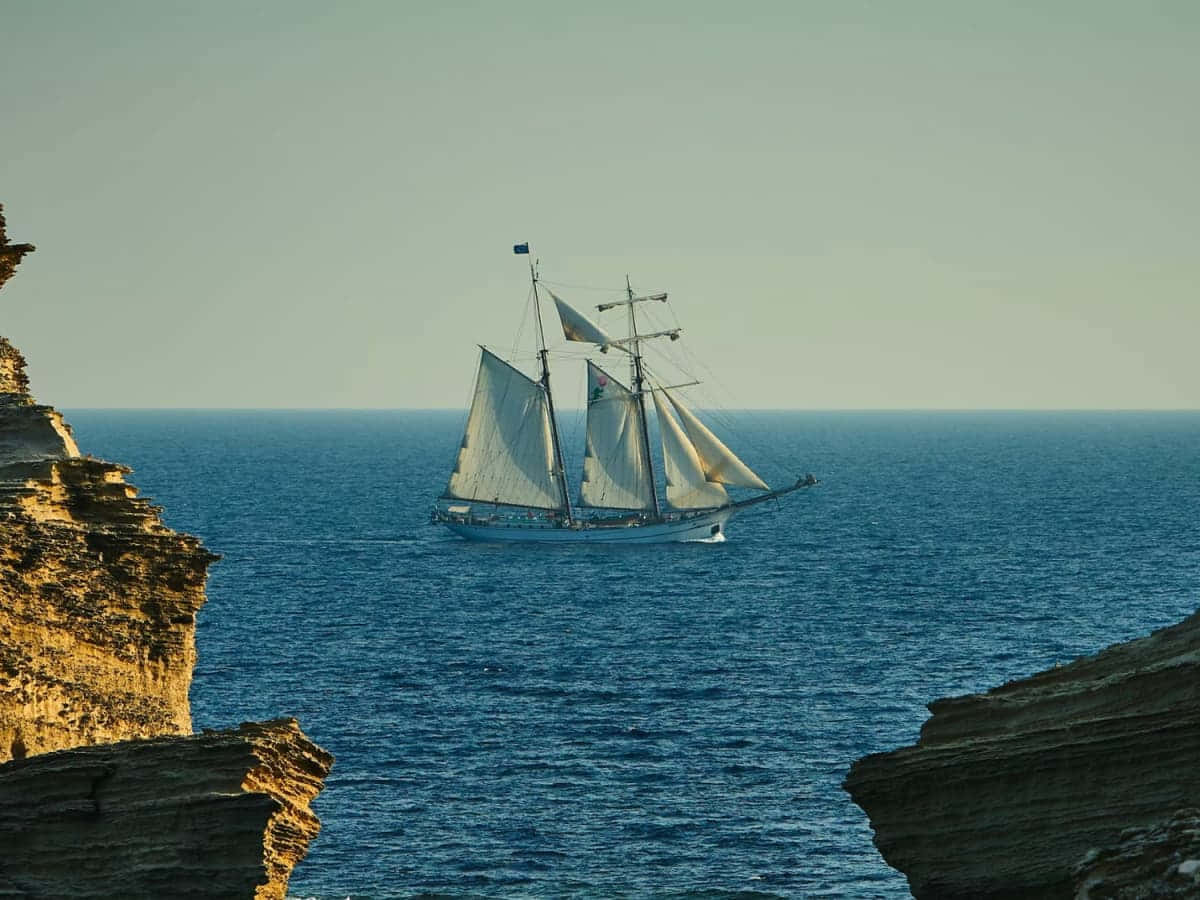 Sailing_ Ship_ Near_ Cliff_ At_ Sunset Wallpaper