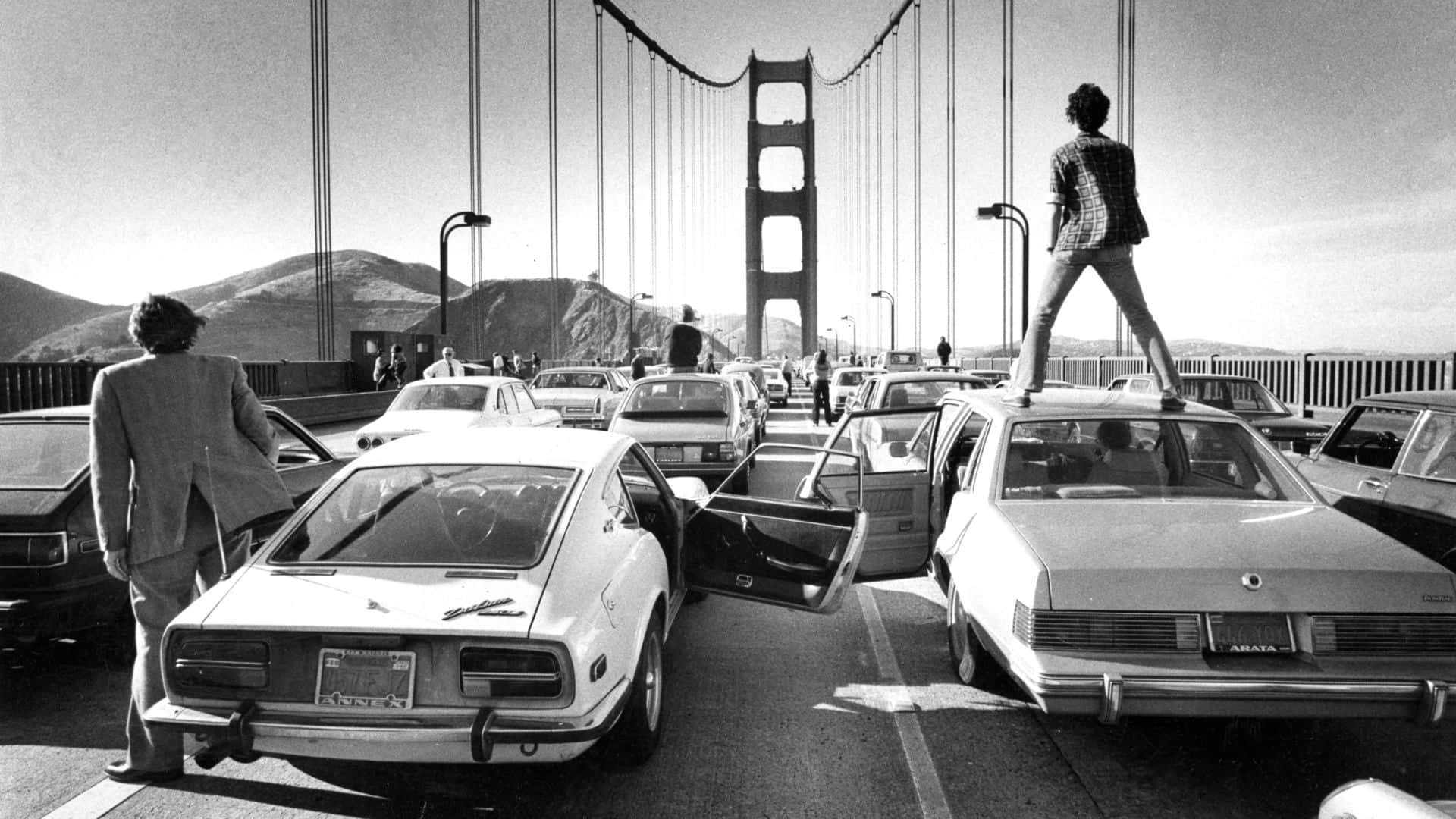 A Man Standing On Top Of A Car On The Golden Gate Bridge Wallpaper