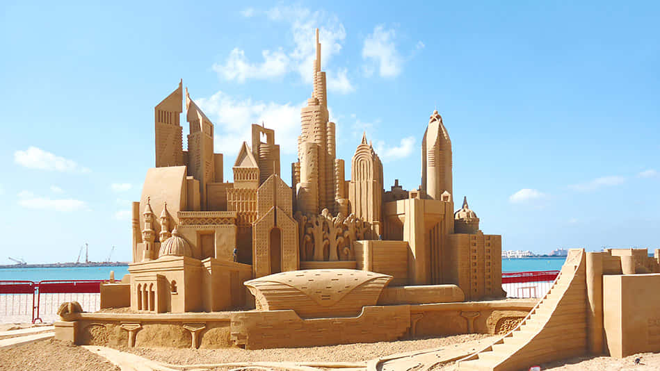 Sand Sculptures On The Beach With A City In The Background
