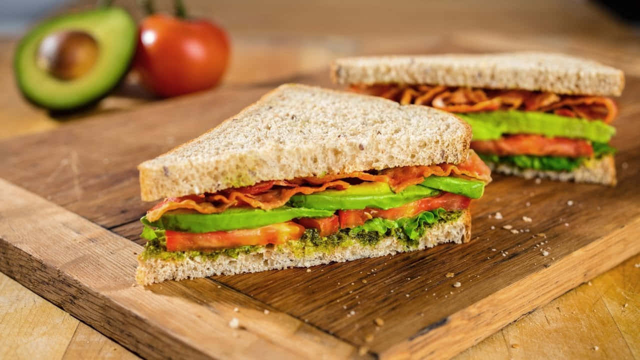 A Sandwich With Avocado, Tomatoes And Bacon On A Cutting Board