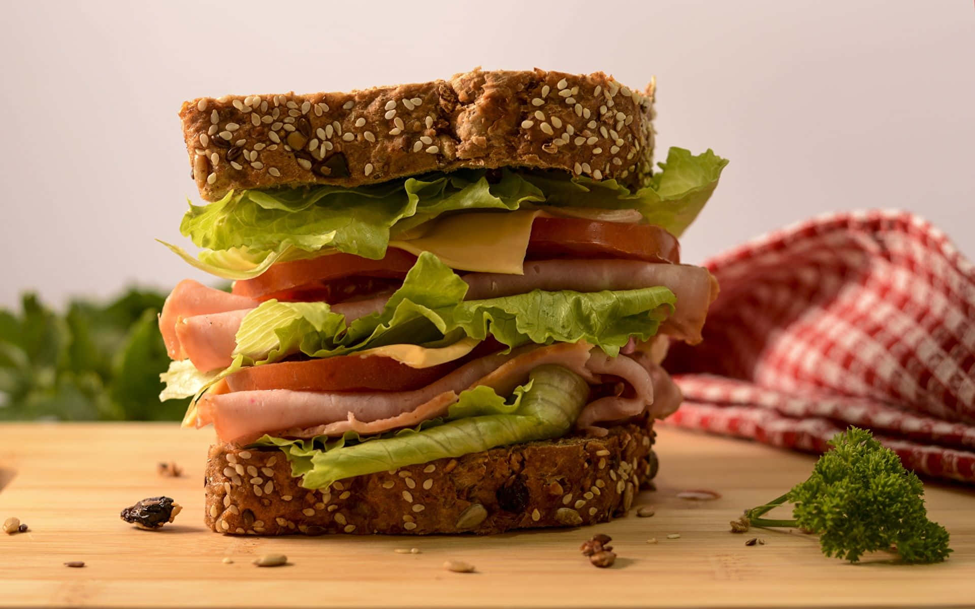 A Sandwich With Ham, Lettuce And Tomatoes On A Wooden Cutting Board
