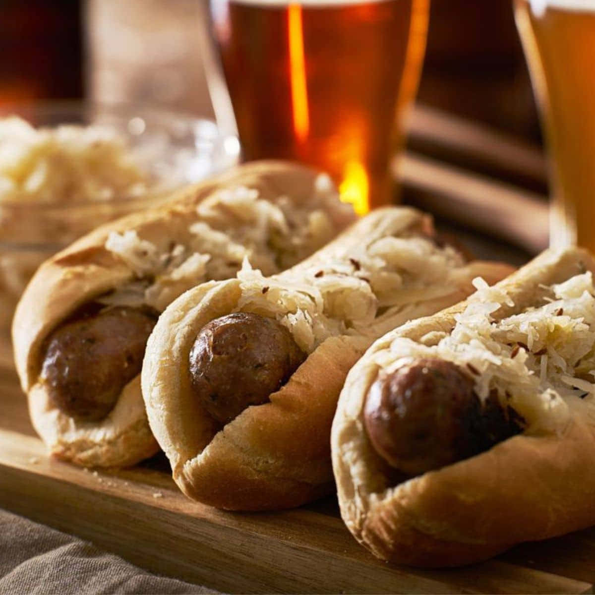 Three Hot Dogs With Sauerkraut And Beer On A Wooden Board